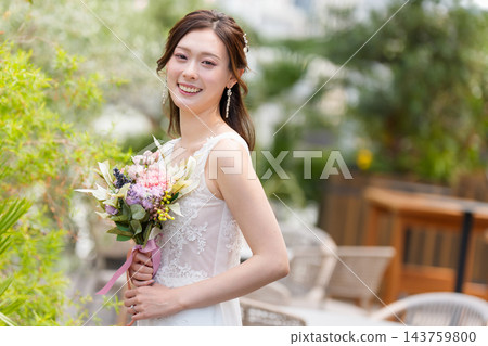 一位身穿婚紗的新娘手捧花束,在露天教堂微笑。 一位身穿婚紗的新娘手捧花束,在露天教堂微笑。 143759800