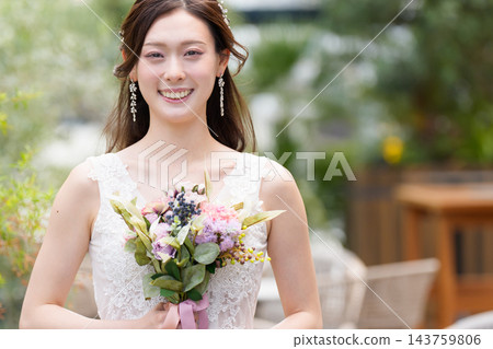 一位身穿婚紗的新娘手捧花束,在露天教堂微笑。 一位身穿婚紗的新娘手捧花束,在露天教堂微笑。 143759806