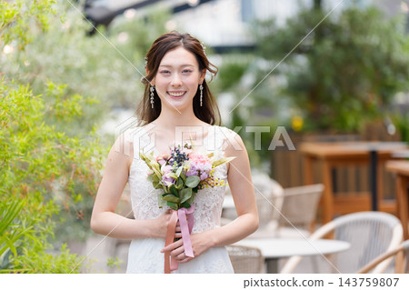 一位身穿婚紗的新娘手捧花束,在露天教堂微笑。 一位身穿婚紗的新娘手捧花束,在露天教堂微笑。 143759807