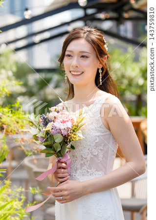 一位身穿婚紗的新娘手捧花束,在露天陽台上微笑。 一位身穿婚紗的新娘手捧花束,在露天陽台上微笑。 143759810