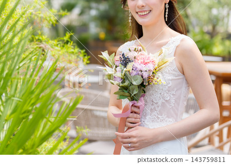 一位身穿婚紗的新娘手捧花束,在露天陽台上微笑。 一位身穿婚紗的新娘手捧花束,在露天陽台上微笑。 143759811