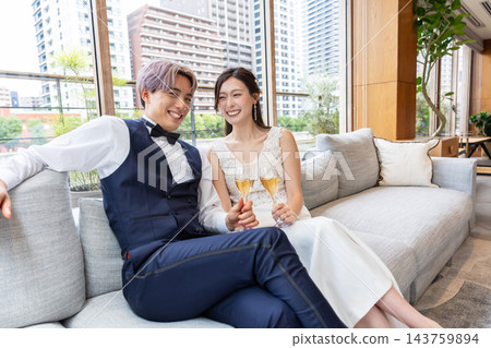 一對笑容滿面的新婚夫婦在休息室的沙發上放鬆休息。 一對笑容滿面的新婚夫婦在休息室的沙發上放鬆休息。 143759894