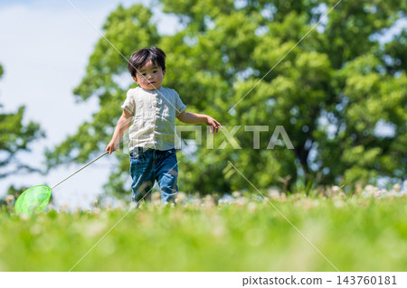 一個男孩拿著捕蝶網,在藍天下的草地上奔跑。 一個男孩拿著捕蝶網,在藍天下的草地上奔跑。 143760181