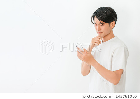 一名二十多歲的男子正在查看智慧型手機上的訊息,陷入沉思,神情焦慮。 一名二十多歲的男子正在查看智慧型手機上的訊息,陷入沉思,神情焦慮。 143761010