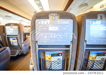 照片顯示,新幹線列車內排列著棕色座椅和折疊桌,座椅背上裝有資訊顯示器和列車雜誌。 照片顯示,新幹線列車內排列著棕色座椅和折疊桌,座椅背上裝有資訊顯示器和列車雜誌。 143761011