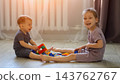 Joyful Siblings Assemble Colorful Toy Bricks Across Living Room Floor, Giggling Cheerfully During Leisure Time While Scattered Small Construction Pieces Represent Possible Home Safety Hazard. 143762767