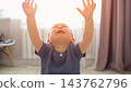 Crying Baby Reaches Arms Upwards Indoors With Distressed Facial Expression. Upset Toddler Sits On Floor Near Window Curtains, Weeping Loudly While Asking For Comfort Under Warm Backlit Glow. 143762796