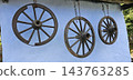 Three weathered wooden wagon wheels hang from rusty chains against a pale blue wall. 143763285