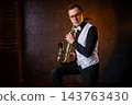 Young man with glasses sitting with golden saxophone 143763430
