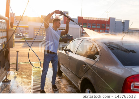 Man rinsing soapy rear window of silver sedan with pressure washer 143763538