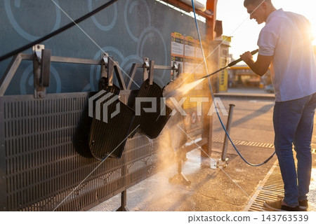 Man washing black floor mats hanging on rack at station Man washing black floor mats hanging on rack at station 143763539