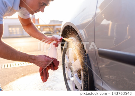 Young man spraying chemical detergent on car tire and wiping rim Young man spraying chemical detergent on car tire and wiping rim 143763543