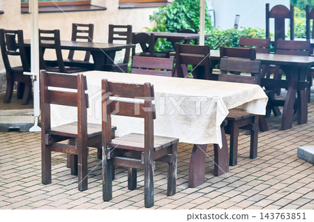 Simple outdoor cafe with heavy wooden tables and chairs Simple outdoor cafe with heavy wooden tables and chairs 143763851