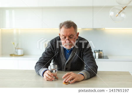 Middle aged senior man holding medical pill and glass of water. Mature old senior grandfather taking medication cure pills vitamin. Age prescription medicine healthcare therapy concept Middle aged senior man holding medical pill and glass of water. Mature old senior grandfather taking medication cure pills vitamin. Age prescription medicine healthcare therapy concept 143765197