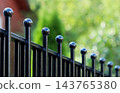 Black wrought iron fence showing decorative ball finials. Pickets providing a sense of enclosure and privacy against green bokeh 143765380