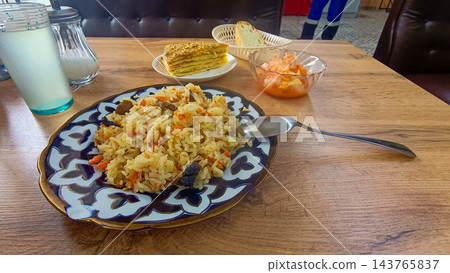 Traditional Uzbek plov pilaf with meat on patterned ceramic plate served on wooden table Traditional Uzbek plov pilaf with meat on patterned ceramic plate served on wooden table 143765837