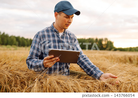 Young Farmer with tablet in the field. Agriculture, gardening or ecology concept. Harvesting Young Farmer with tablet in the field. Agriculture, gardening or ecology concept. Harvesting 143766054