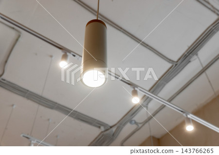 A glowing pendant light hangs from a white ceiling with track lighting A glowing pendant light hangs from a white ceiling with track lighting 143766265