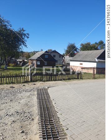 Rural mountain village street with traditional wooden houses, a rustic picket fence and paving stones under a clear blue sky. Carpathian countryside on a sunny autumn day, travel 143766315