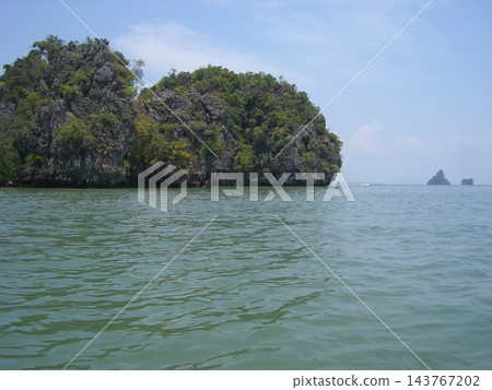 在泰國攀牙灣,一座鬱鬱蔥蔥、岩石嶙峋的小島漂浮在藍天之下。 在泰國攀牙灣,一座鬱鬱蔥蔥、岩石嶙峋的小島漂浮在藍天之下。 143767202