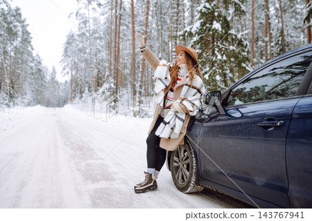 Beautiful young woman near a car in a snowy forest. First snow, great mood. Concept of vacation. Beautiful young woman near a car in a snowy forest. First snow, great mood. Concept of vacation. 143767941