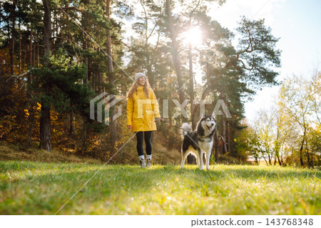 Young woman walks with her husky on lawn in the park. Happy female posing outdoors with her dog. Young woman walks with her husky on lawn in the park. Happy female posing outdoors with her dog. 143768348