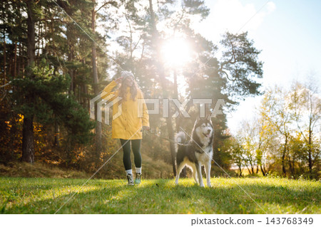 Young woman walks with her husky on lawn in the park. Happy female posing outdoors with her dog. 143768349