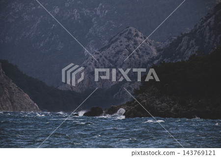 Storm Waves Crashing Against Rocky Cliffs Near a Forest. 143769121
