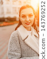 Woman sunset coat smiling outdoors in urban environment during warm golden hour with copy space 143769252