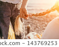 Braid hair beach setting with hands holding long blonde hair on pebble shore under warm sunset light 143769253