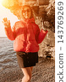Woman winter jacket young lady standing on pebble beach near cliff during golden hour sunset with copy space 143769269