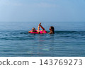 Family beach swimming mother and daughter play with a pink inflatable ring in the calm blue sea during a sunny summer vacation 143769273
