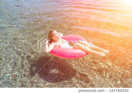 Woman floating beach young lady relaxes on a pink inflatable ring in crystal clear sea water during a sunny summer vacation 143769292
