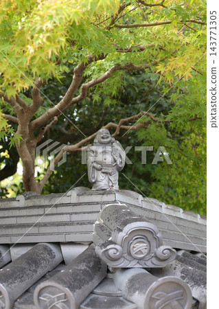 一座日本建築的瓦片屋頂上放置著七福神之一布袋和尚的石像。 一座日本建築的瓦片屋頂上放置著七福神之一布袋和尚的石像。 143771305