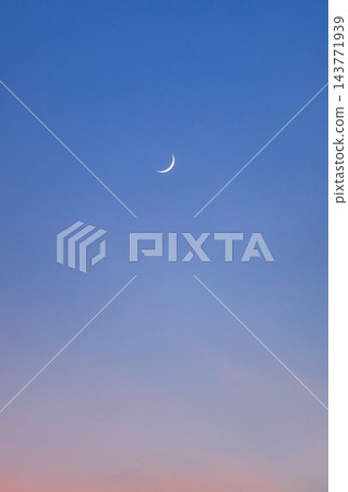 A slender crescent moon glows in a deep blue twilight sky above a softly colored horizon A slender crescent moon glows in a deep blue twilight sky above a softly colored horizon 143771939