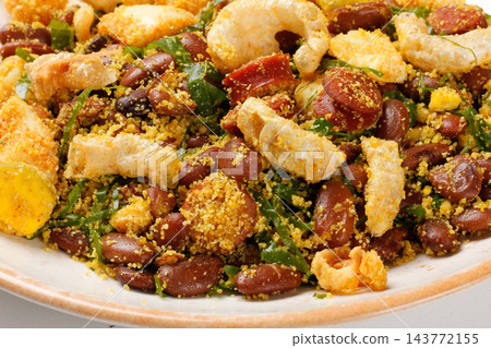 Close up of traditional Brazilian feijao tropeiro served on a rustic ceramic plate. Front view. Close up of traditional Brazilian feijao tropeiro served on a rustic ceramic plate. Front view. 143772155