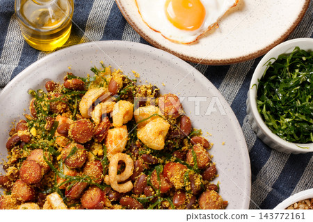 Brazilian feijao tropeiro with sausage, pork rinds and eggs served on a rustic plate on a tablecloth covered table. 143772161