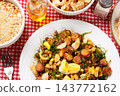 Brazilian feijao tropeiro with sausage, pork rinds and eggs served on a white ceramic plate on a table with a checkered tablecloth. 143772162