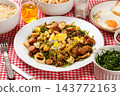 Brazilian feijao tropeiro with sausage, pork rinds and eggs served on a white ceramic plate on a table with a checkered tablecloth. 143772163