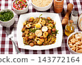 Brazilian feijao tropeiro with sausage, pork rinds and eggs served on a white square plate on a table with a checkered tablecloth. 143772164