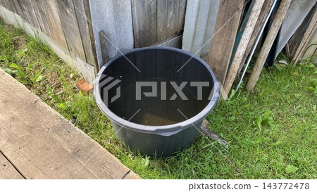 Black plastic water container for rainwater collection in a rural garden Black plastic water container for rainwater collection in a rural garden 143772478