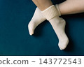 Woman crossing legs in white socks. Girl legs in cozy wool socks on blue background. Cozy autumn lifestyle. Woven socks on woman legs. Woman holding feet on blue sofa. Winter fashion. 143772543