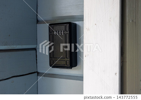 Secure outdoor key lock box mounted on wooden house wall for safe spare key storage and property access 143772555