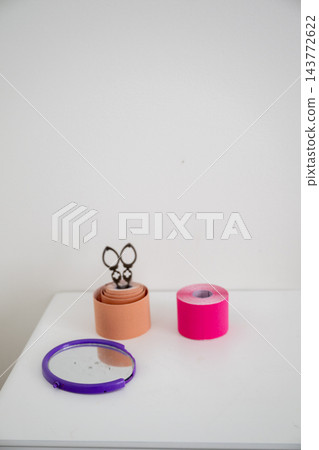 Colorful kinesiology tape rolls with hand mirror and massage scraper on white tabletop 143772622