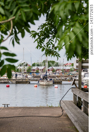 peaceful marina scene with sailboats docked at a wooden dockside perspective in a harbor setting with green and white surroundings and a serene atmosphere for travel and recreation. peaceful marina scene with sailboats docked at a wooden dockside perspective in a harbor setting with green and white surroundings and a serene atmosphere for travel and recreation. 143772655