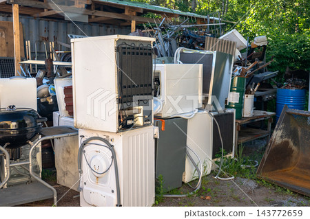 Discarded household appliances and electronic waste at outdoor recycling center awaiting processing Discarded household appliances and electronic waste at outdoor recycling center awaiting processing 143772659