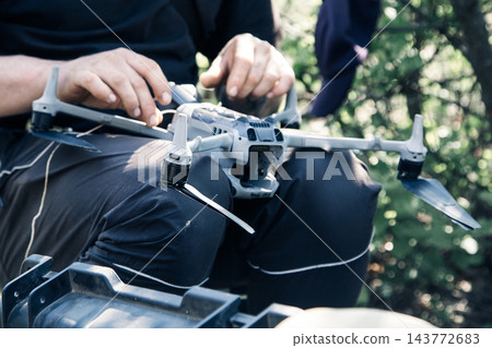 Person inspecting or preparing a quadcopter drone outdoors 143772683