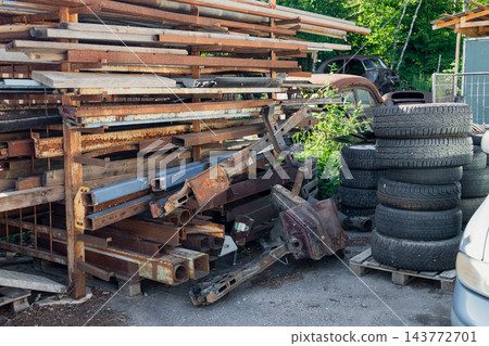 Rusty metal stockpile with discarded car parts and stacked tires in automotive salvage yard 143772701