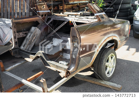 Rusty classic car body shell on restoration stand in automotive workshop before repair and rebuilding Rusty classic car body shell on restoration stand in automotive workshop before repair and rebuilding 143772713