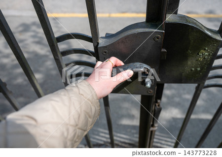 Closeup of hand opening black wrought iron gate on sunny urban street with selective focus and minimal composition 143773228